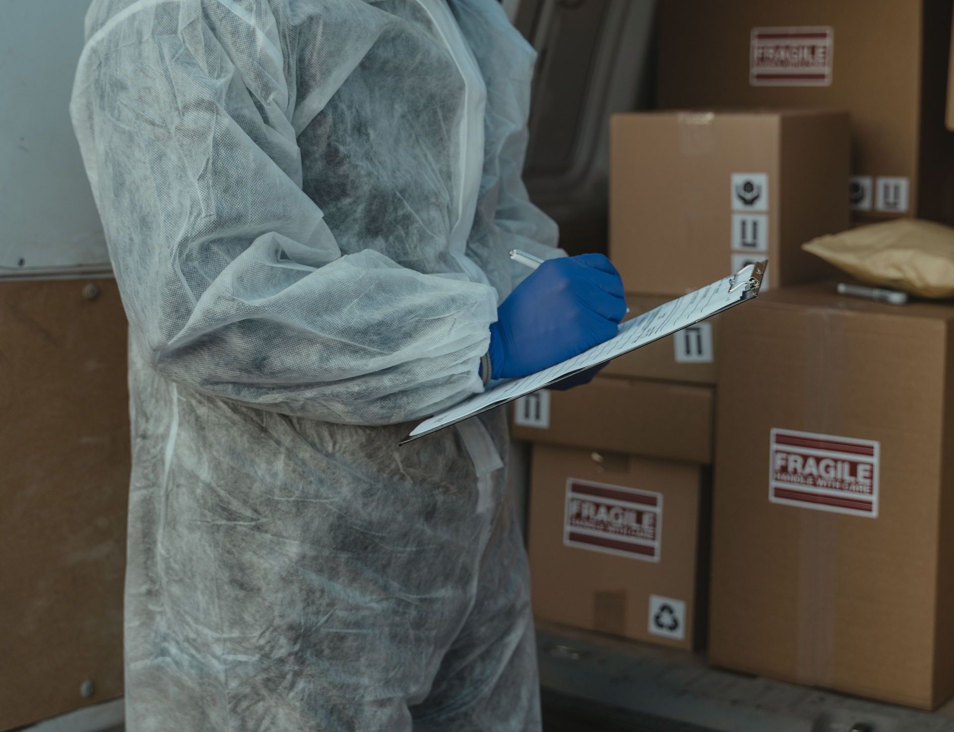 A logistics worker in PPE inspects packages in a delivery van for shipment.
